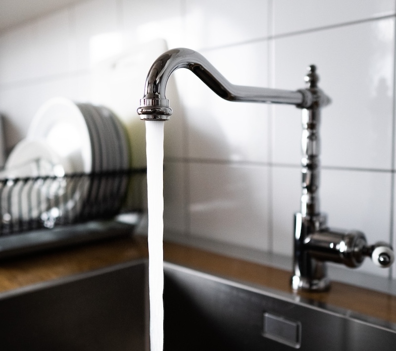 A stainless steel kitchen faucet is streaming water into a kitchen sink.
